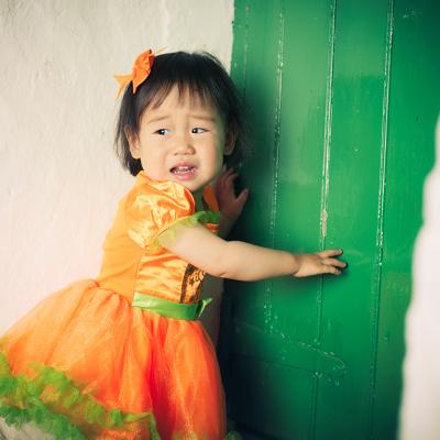 A young girl wearing an orange Halloween dress crying during a party.