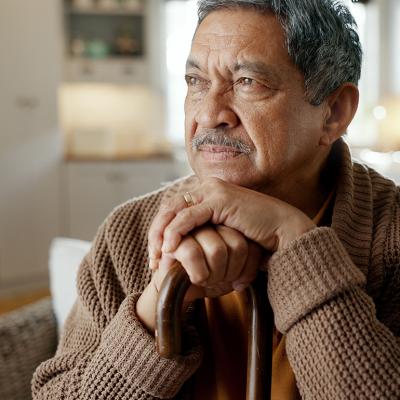A senior man with a cane thinks deeply while sitting on a sofa.