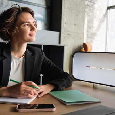 Business woman in office looks toward window thinking while taking notes.