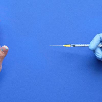 A hand refusing to receive a vaccine syringe.