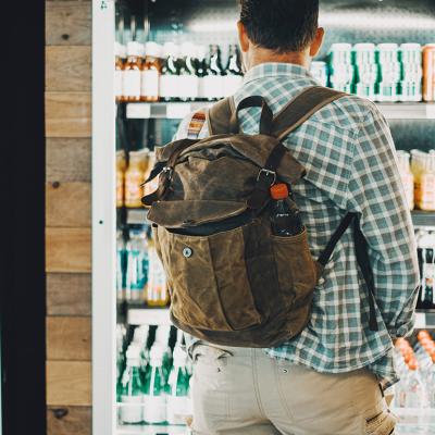 A man traveling with a backpack facing the cold drinks section of an airport food store.