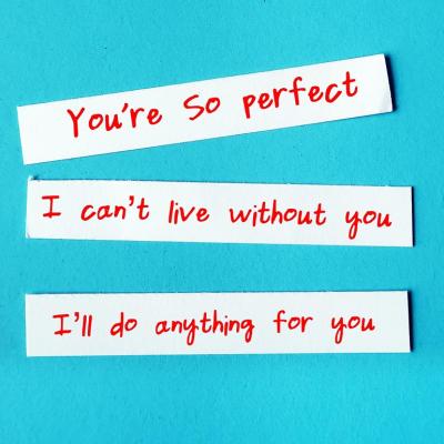 Love bombing messages written on slips of paper such as "I can't live without you," photographed against turquoise background.