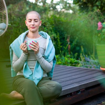 A breast cancer patient sitting on a garden patio with a cup of coffee in her hands.