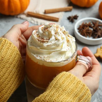 Closeup on a woman holding a cup of pumpkin spice latte with whipped cream.