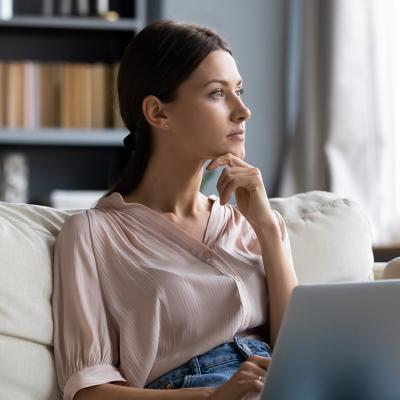 A young woman at home contemplating on couch while using laptop.