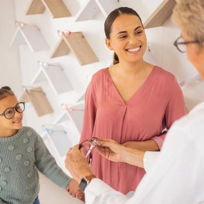 Girl with mother trying on glasses at an eyewear store talking to specialist. 