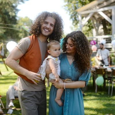 A happy couple pose with their baby at a backyard party.