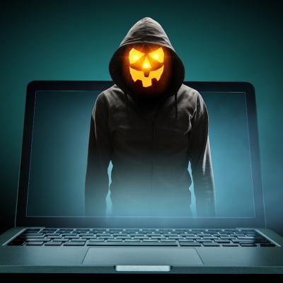 Anonymous man with a Halloween pumpkin head illustrated as emerging from a laptop.