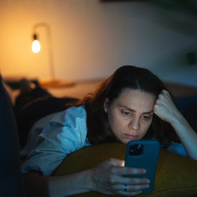 A serious young woman lying on a sofa and scrolling through her phone.