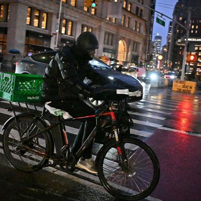 A rider transports a delivery using an e-bike on a street in midtown Manhattan on a rainy night on December 22, 2024 in New York City, USA. 