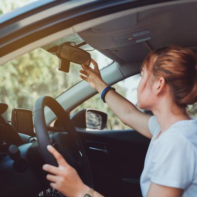 A woman adjusts her car's rearview mirror before driving.