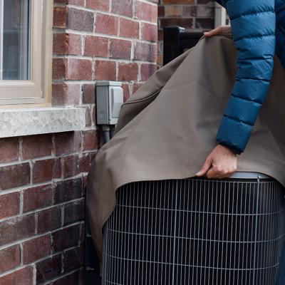 A woman covers their air conditioning unit set outside the house.