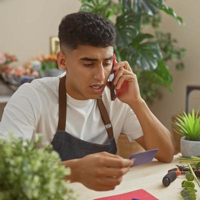 A flower shop business owner holding a credit card while talking on the phone.