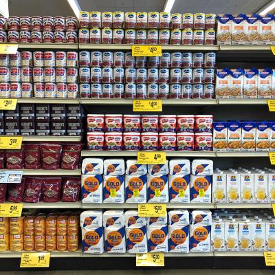 Grocery store shelves of common Thanksgiving and Christmas dinner supplies such as cans of condensed milk, pumpkin puree, and cranberry sauce.