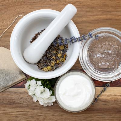 A top view of natural beauty ingredients on a table such as a tea bag, face cream and soap, and a mortar and pestle with dried flowers.