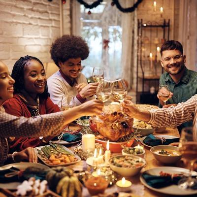 Group of diverse young people toasting at dining table while celebrating Thanksgiving at home. 