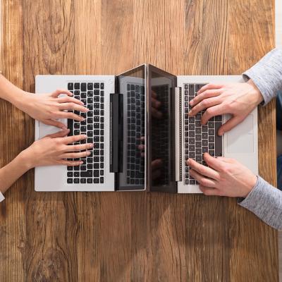An overhead view of two people using laptops and sitting across each other on a table.
