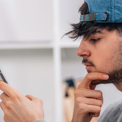 A young man looks at his smartphone pensively.