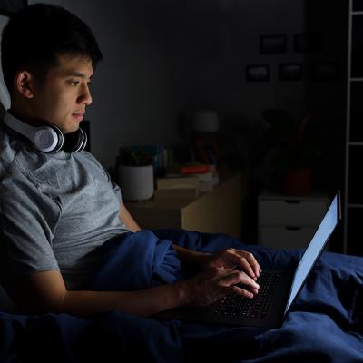 A young man uses his laptop in bed at night.