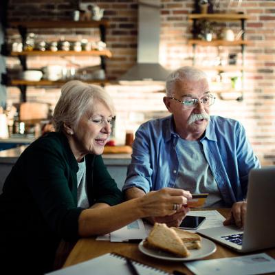 An elderly couple using a credit card at home with a laptop.
