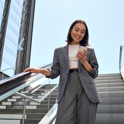 A young female marketing professional smiling at her phone while standing on an escalator.