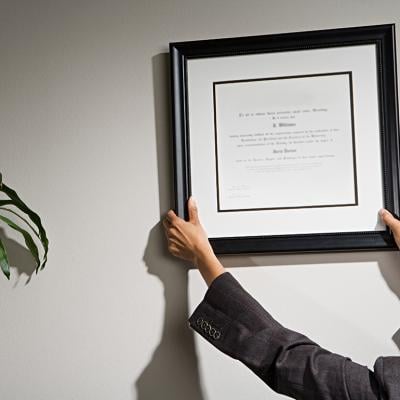 A business woman hanging a framed diploma.