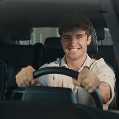 A young man with a big grin sits happily inside a new car.