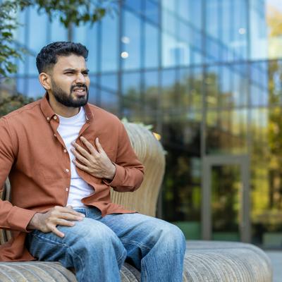 A young man nervously sitting on a bench outdoors experiencing chest pains.