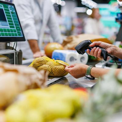 A supermarket cashier staff scans a bag of potatoes at a checkout counter.