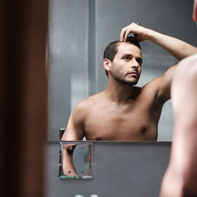 A man looks himself at the mirror inspecting his receding hairline.