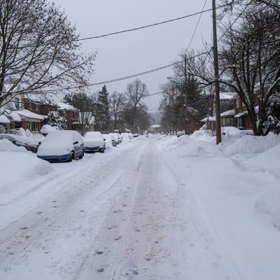 Unplowed snow accumulated on a residential street where rows of cars are parked.