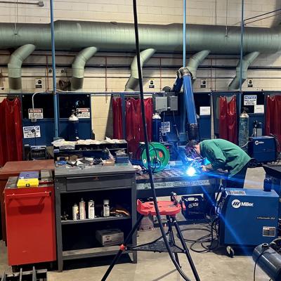 A welding demonstration taking place at a summer program in Philadelphia, colorful stations are in the background. 