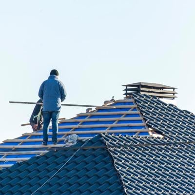 Workers installing metal tile on the roof while roofing house in construction site.