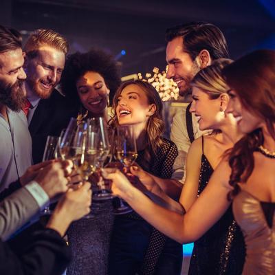 A group of people in party dresses and suits clink glasses together in a party setting.