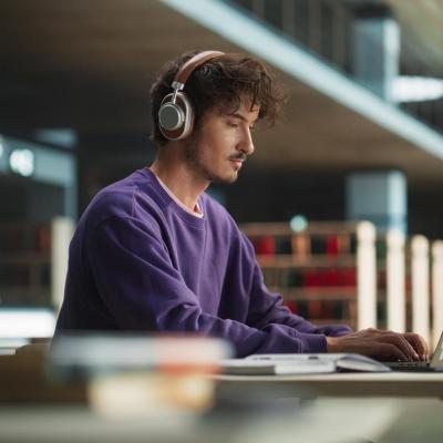Person wearing purple sweatshirt and phones working on laptop in library. 