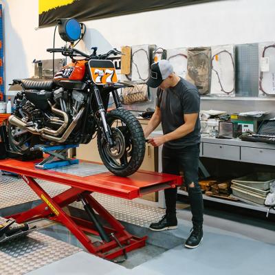 Unrecognizable mechanic man checking engine of custom motorcycle over platform.