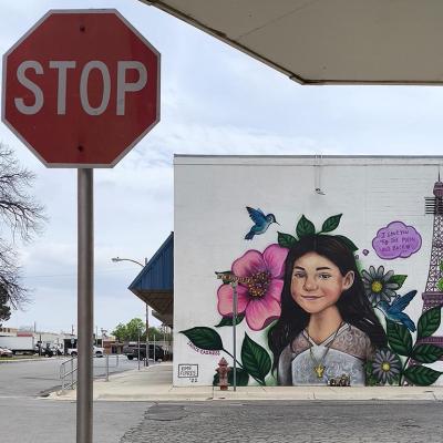 A murals of shooting victims in Uvalde painted on a wall behind a stop sign.