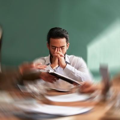 A male employee seated at the center of an office table with his surroundings are illustrated with a motion blur.