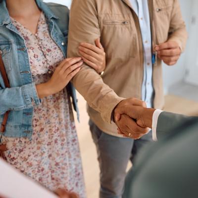 A couple shaking hands with a real estate agent after purchase.