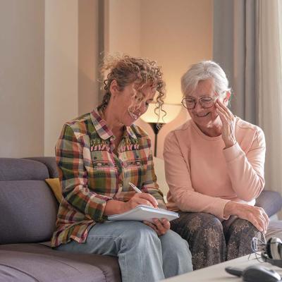A senior woman and her caregiver sitting together on a sofa at home.