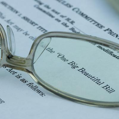 A pair of eyeglasses magnified on the words 'One Big Beautiful Bill' (Act) on a document.