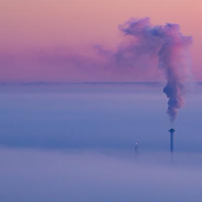 Smoke coming out of a heat and power plant chimney, blending with a lavender morning sky.