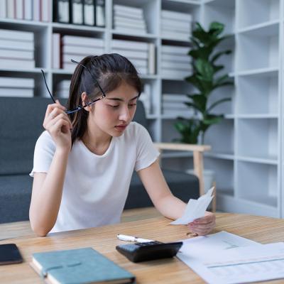 A confused young woman reviewing financial documents at her home office.