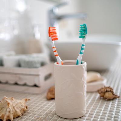 Two colorful toothbrushes in a ceramic glass against the background of a bathroom's washbasin.