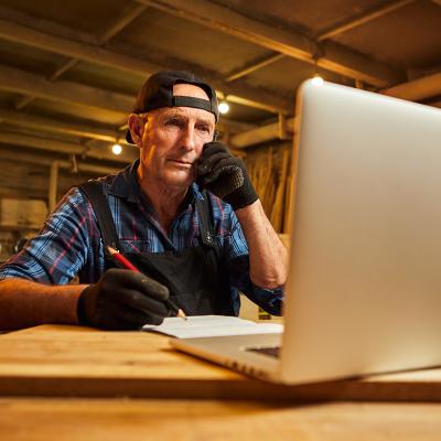 A senior male carpenter working with a client online from their workshop.