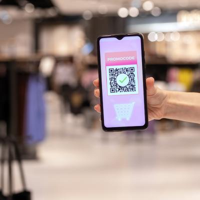 A woman's hand holding a phone displaying promo code applied by scanning a QR code inside a shopping mall.