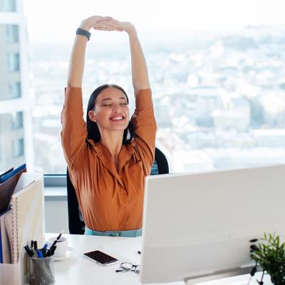 A female manager happily stretching her back and arms while seated at her desk in an office.