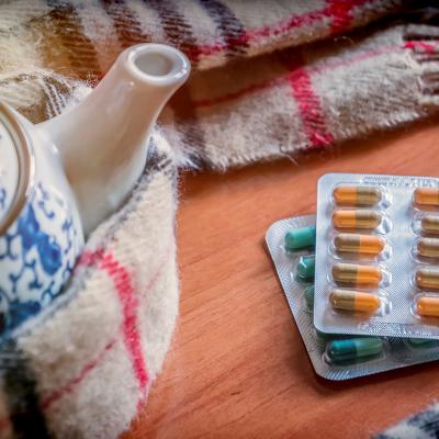 Sheets of pills beside a teapot wrapped in scarf.