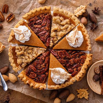 A pie composed of alternating slices of pumpkin with whipped cream and pecan pie, on parchment paper. 