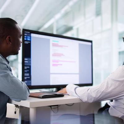 Two people sitting at a desk looking at a large screen; one is a privacy compliance specialist ensuring HIPAA regulations are being followed correctly.